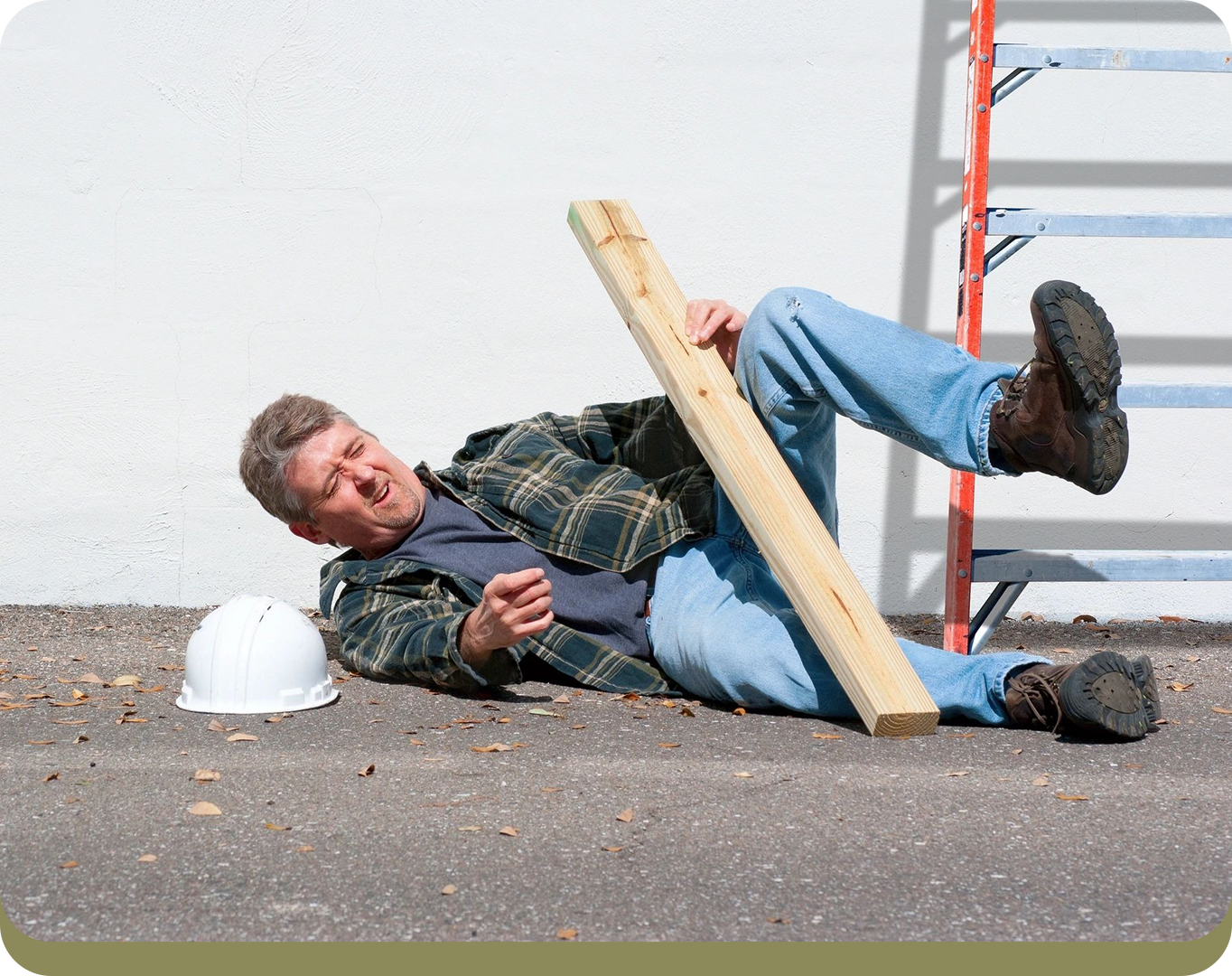 A man wearing a plaid shirt and jeans falls on the pavement while holding a wooden plank. A white hard hat lies beside him, and a red and silver ladder is visible in the background.