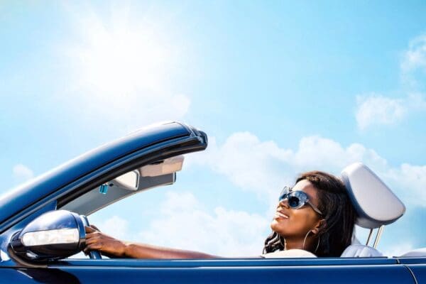 A woman driving in her blue car with the sun shining on it.